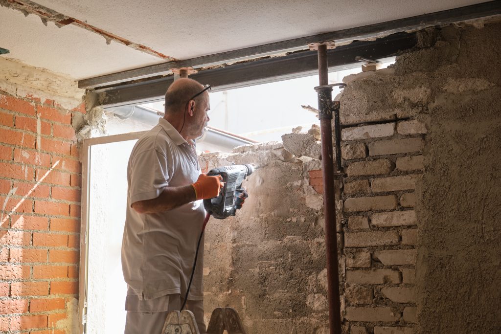 Trabajador de la construcción con un martillo neumático de demolición rompiendo una pared interior.