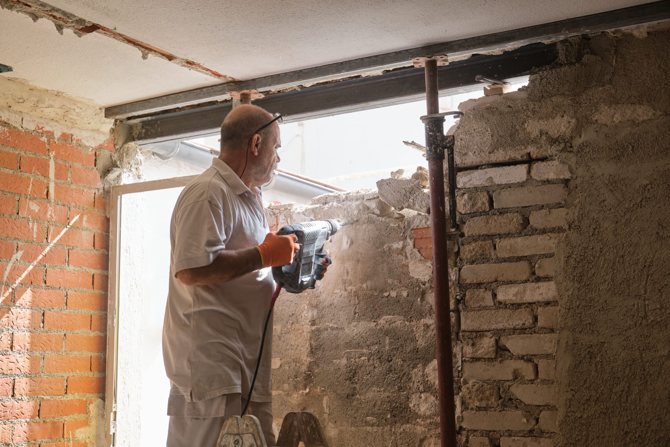 Trabajador de la construcción con un martillo neumático de demolición rompiendo una pared interior.